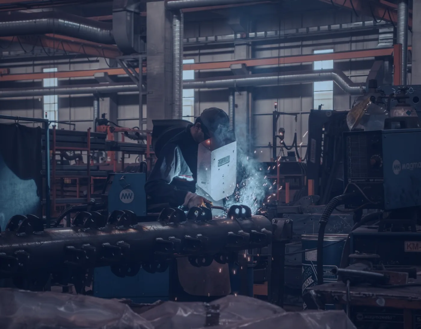 Welder working on steel parts on a factory floor at night